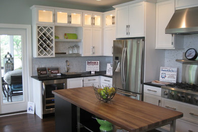 Beach style l-shaped dark wood floor eat-in kitchen photo in Grand Rapids with a farmhouse sink, glass-front cabinets, white cabinets, wood countertops, glass tile backsplash, stainless steel appliances and an island