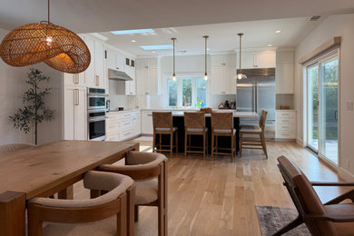 Large transitional l-shaped medium tone wood floor and brown floor open concept kitchen photo in San Francisco with an undermount sink, recessed-panel cabinets, white cabinets, quartz countertops, white backsplash, quartz backsplash, stainless steel appliances, an island and white countertops