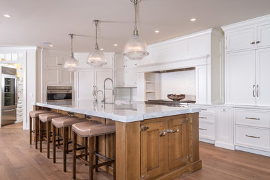 Photo of a large beach style single-wall open plan kitchen in Los Angeles with an integrated sink, white splashback, panelled appliances, white cabinets, medium hardwood floors, recessed-panel cabinets, marble benchtops, with island and brown floor.