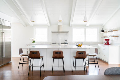 Inspiration for a beach style l-shaped eat-in kitchen in Boston with flat-panel cabinets, white cabinets, white splashback, stone slab splashback, stainless steel appliances, medium hardwood floors, with island and white benchtop.