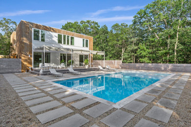 This is an example of a medium sized modern back rectangular swimming pool in New York with concrete slabs.