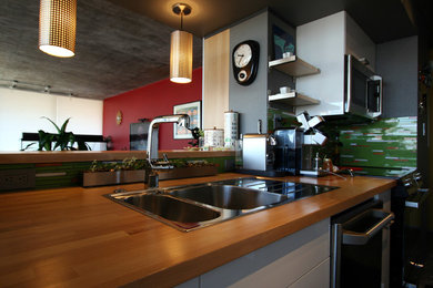 Inspiration for a small contemporary galley concrete floor open concept kitchen remodel in Other with a drop-in sink, flat-panel cabinets, white cabinets, wood countertops, green backsplash, glass tile backsplash, stainless steel appliances and a peninsula