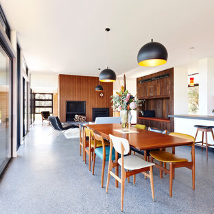 Contemporary open plan dining in Melbourne with white walls, a standard fireplace, a wood fireplace surround and grey floor.