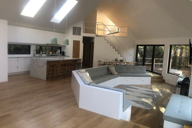 Family room - large modern open concept light wood floor, brown floor and vaulted ceiling family room idea in New York with white walls, a wall-mounted tv, a standard fireplace and a brick fireplace