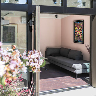 Small modern home studio in Los Angeles with pink walls, vinyl flooring, a built-in desk and brown floors.