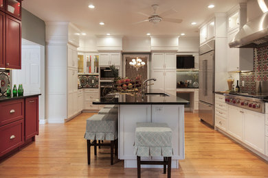 This is an example of a large transitional u-shaped separate kitchen in St Louis with white cabinets, shaker cabinets, with island, granite benchtops, an undermount sink, red splashback, ceramic splashback, stainless steel appliances, light hardwood floors, brown floor and black benchtop.