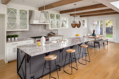 Inspiration for a large cottage single-wall light wood floor, brown floor and exposed beam eat-in kitchen remodel in Orange County with an undermount sink, glass-front cabinets, white cabinets, gray backsplash, ceramic backsplash, stainless steel appliances, an island and gray countertops
