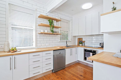 Inspiration for a mid-sized u-shaped eat-in kitchen in Newcastle - Maitland with a single-bowl sink, flat-panel cabinets, white cabinets, wood benchtops, white splashback, subway tile splashback, stainless steel appliances, medium hardwood floors and no island.