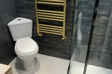 Design ideas for a small modern ensuite bathroom in Cambridgeshire with flat-panel cabinets, light wood cabinets, a corner shower, a two-piece toilet, black tiles, a vessel sink, laminate worktops, a sliding door, a feature wall, a single sink and a floating vanity unit.