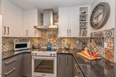 Example of a mid-sized transitional u-shaped light wood floor and brown floor enclosed kitchen design in Vancouver with a double-bowl sink, flat-panel cabinets, white cabinets, granite countertops, multicolored backsplash, ceramic backsplash, white appliances and a peninsula