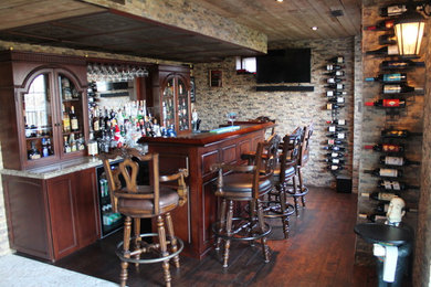 Large tuscan single-wall dark wood floor seated home bar photo in Toronto with a drop-in sink, glass-front cabinets, brown cabinets, granite countertops, beige backsplash and stone tile backsplash