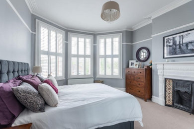 Medium sized contemporary master bedroom in London with grey walls, carpet, a standard fireplace, a tiled fireplace surround and beige floors.