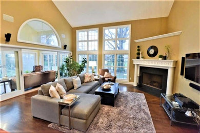 Example of a huge transitional enclosed and formal medium tone wood floor and brown floor living room design in Columbus with beige walls, a corner fireplace, a plaster fireplace and a wall-mounted tv