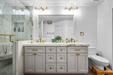 Mid-sized transitional master multicolored tile and marble tile medium tone wood floor, brown floor and double-sink corner shower photo in Dallas with recessed-panel cabinets, gray cabinets, a two-piece toilet, white walls, an undermount sink, marble countertops, a hinged shower door, white countertops and a built-in vanity