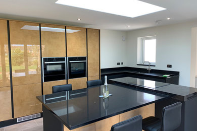 Design ideas for a medium sized modern grey and black l-shaped kitchen/diner in Essex with a built-in sink, flat-panel cabinets, dark wood cabinets, quartz worktops, black splashback, engineered quartz splashback, integrated appliances, vinyl flooring, an island, grey floors and black worktops.