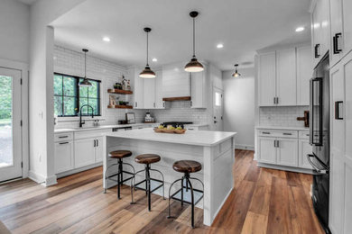 Example of a cottage eat-in kitchen design in New York with a double-bowl sink, shaker cabinets, white cabinets, white backsplash, subway tile backsplash, black appliances, an island and white countertops