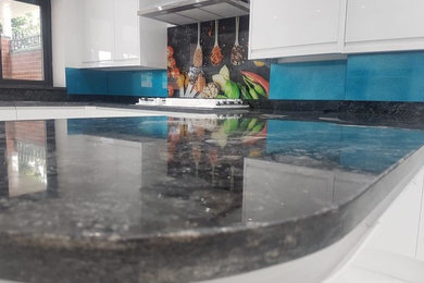 Foto di una cucina abitabile moderna con ante lisce, ante bianche, top in marmo, paraspruzzi blu, paraspruzzi con lastra di vetro e top nero