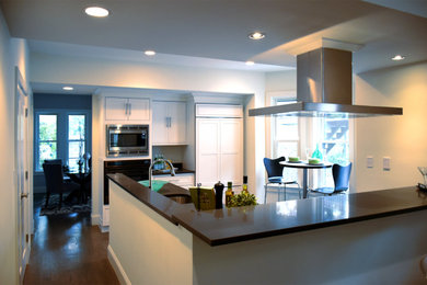 Example of a mid-sized minimalist l-shaped dark wood floor and gray floor eat-in kitchen design with an undermount sink, flat-panel cabinets, white cabinets, granite countertops, black backsplash, stone tile backsplash, stainless steel appliances, a peninsula and black countertops