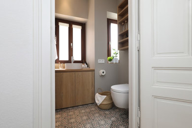 Photo of a small modern 3/4 bathroom in Frankfurt with flat-panel cabinets, light wood cabinets, a built-in vanity, an alcove shower, a two-piece toilet, grey walls, cement tiles, a vessel sink, wood benchtops, multi-coloured floor, an open shower, a single vanity, wallpaper and wallpaper.