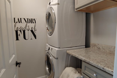 Small trendy single-wall ceramic tile and beige floor dedicated laundry room photo in Other with shaker cabinets, gray cabinets, laminate countertops, gray walls, a stacked washer/dryer and gray countertops