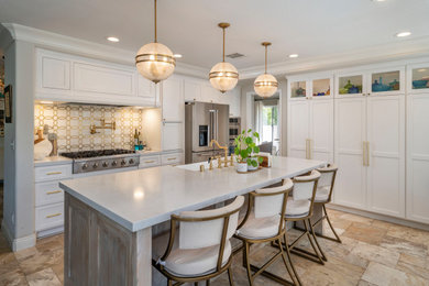 Example of a classic u-shaped travertine floor and beige floor kitchen design with shaker cabinets, white cabinets, quartz countertops, marble backsplash, stainless steel appliances, an island and white countertops