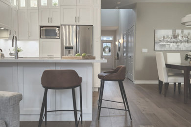 Inspiration for a large transitional medium tone wood floor, brown floor and vaulted ceiling open concept kitchen remodel in Toronto with a drop-in sink, shaker cabinets, white cabinets, quartz countertops, white backsplash, porcelain backsplash, stainless steel appliances and white countertops