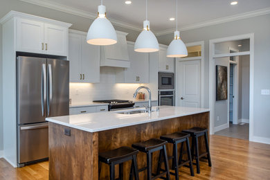Mid-sized transitional galley medium tone wood floor and brown floor open concept kitchen photo in Other with a double-bowl sink, shaker cabinets, white cabinets, white backsplash, subway tile backsplash, stainless steel appliances, an island and white countertops