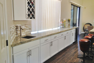 Example of a mid-sized trendy single-wall brown floor wet bar design in Phoenix with an undermount sink, shaker cabinets, white cabinets, granite countertops, beige backsplash and glass tile backsplash