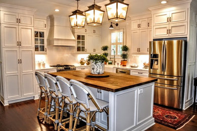 Mid-sized traditional l-shaped open plan kitchen in Atlanta with a farmhouse sink, beaded inset cabinets, white cabinets, wood benchtops, white splashback, subway tile splashback, stainless steel appliances, dark hardwood floors, with island and brown floor.
