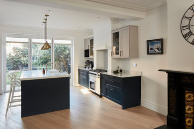 Inspiration for a large transitional kitchen in London with a farmhouse sink, shaker cabinets, blue cabinets, quartzite benchtops, grey splashback, engineered quartz splashback, stainless steel appliances, light hardwood floors, with island, brown floor and grey benchtop.