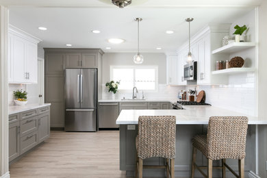 Photo of a medium sized traditional u-shaped kitchen/diner in Los Angeles with a submerged sink, shaker cabinets, beige cabinets, engineered stone countertops, white splashback, ceramic splashback, stainless steel appliances, a breakfast bar, beige floors and white worktops.