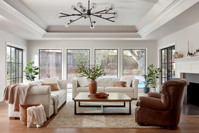 Example of a large arts and crafts enclosed medium tone wood floor, brown floor and tray ceiling living room design in San Francisco with beige walls, a standard fireplace and a wood fireplace surround