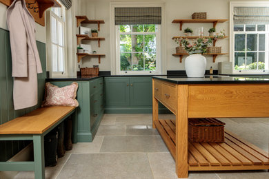 This is an example of a large traditional l-shaped utility room in Berkshire with a belfast sink, shaker cabinets, green cabinets, granite worktops, white walls, limestone flooring, a side by side washer and dryer, beige floors and black worktops.