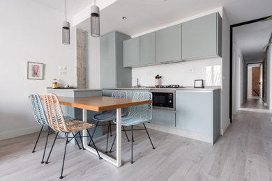 Modelo de cocina nórdica de tamaño medio con armarios con paneles lisos, puertas de armario grises, salpicadero blanco, salpicadero de vidrio templado, electrodomésticos de acero inoxidable, suelo de madera clara, península, suelo gris y encimeras grises