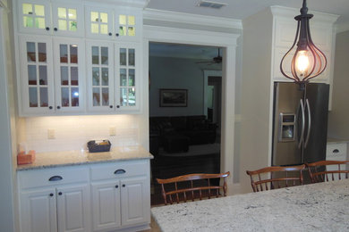 Inspiration for a timeless kitchen remodel in Little Rock with a farmhouse sink, raised-panel cabinets, white cabinets, granite countertops, white backsplash, subway tile backsplash, stainless steel appliances and an island