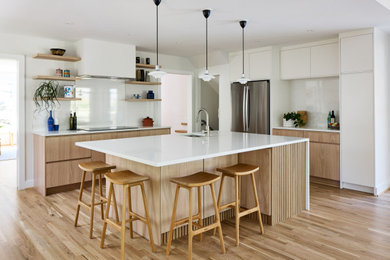 Example of a large trendy u-shaped light wood floor and brown floor open concept kitchen design in DC Metro with an undermount sink, flat-panel cabinets, light wood cabinets, white backsplash, stainless steel appliances, an island and white countertops