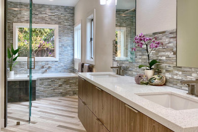 Example of a large trendy master gray tile and glass tile wood-look tile floor, multicolored floor and double-sink bathroom design in San Francisco with flat-panel cabinets, medium tone wood cabinets, an undermount tub, beige walls, an undermount sink, quartz countertops, a hinged shower door, white countertops and a floating vanity
