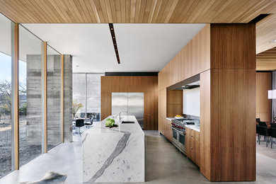 Inspiration for a large modern concrete floor and gray floor open concept kitchen remodel in Austin with flat-panel cabinets, medium tone wood cabinets, an island, an undermount sink, stainless steel appliances and white countertops