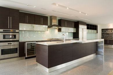 Example of a 1960s galley kitchen design in Tampa with an undermount sink, flat-panel cabinets, dark wood cabinets, white backsplash and stainless steel appliances