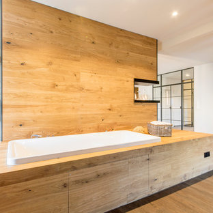 Cette image montre une grande salle d'eau chalet avec une baignoire posée, un sol en vinyl, un sol marron, aucune cabine, un mur blanc, un combiné douche/baignoire et un WC suspendu.