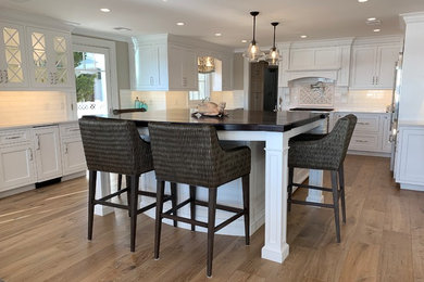 Eat-in kitchen - large transitional light wood floor and brown floor eat-in kitchen idea in Other with recessed-panel cabinets, white cabinets, white backsplash, porcelain backsplash, stainless steel appliances, an island and white countertops