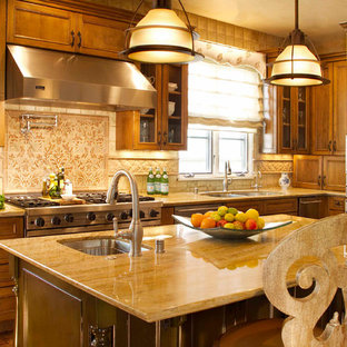 Design ideas for a mediterranean l-shaped kitchen pantry with a double-bowl sink, recessed-panel cabinets, brown cabinets, beige splashback, terra-cotta splashback, stainless steel appliances, medium hardwood floors, with island, brown floor, beige benchtop and limestone benchtops.