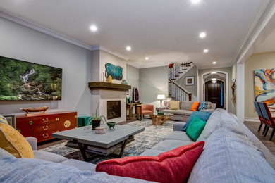 Источник вдохновения для домашнего уюта: большая открытая гостиная комната в классическом стиле с серыми стенами, паркетным полом среднего тона, стандартным камином, фасадом камина из плитки, телевизором на стене и серым полом