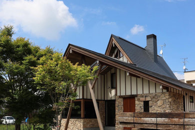 Foto de fachada de casa beige y negra de tamaño medio de dos plantas con revestimiento de piedra, tejado a dos aguas y tejado de metal