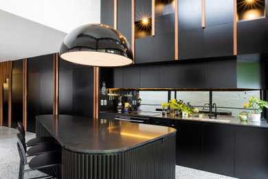 Photo of a mid-sized contemporary single-wall kitchen in Other with a drop-in sink, shaker cabinets, black cabinets, quartz benchtops, black splashback, mirror splashback, black appliances, terrazzo floors, with island, grey floor and black benchtop.