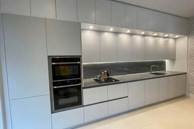 Medium sized contemporary grey and white single-wall kitchen/diner in London with a submerged sink, flat-panel cabinets, grey cabinets, granite worktops, grey splashback, granite splashback, stainless steel appliances, porcelain flooring, no island, beige floors, grey worktops, a drop ceiling and feature lighting.