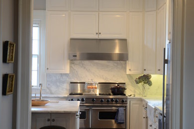 Inspiration for a large timeless u-shaped medium tone wood floor enclosed kitchen remodel in Other with a farmhouse sink, raised-panel cabinets, white cabinets, marble countertops, white backsplash, stone slab backsplash, stainless steel appliances and an island