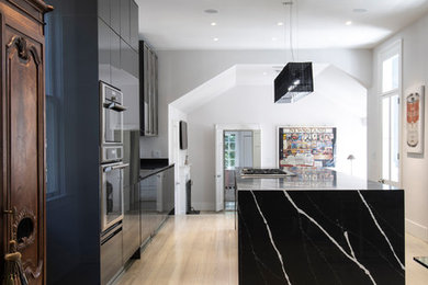 Large trendy galley light wood floor open concept kitchen photo in Charleston with an undermount sink, flat-panel cabinets, black cabinets, quartz countertops, metallic backsplash, metal backsplash, paneled appliances, an island and black countertops