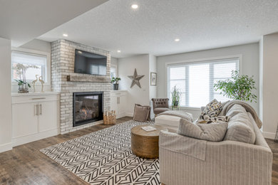 Transitional open concept medium tone wood floor and brown floor living room photo in Calgary with a standard fireplace, a brick fireplace, beige walls and a wall-mounted tv