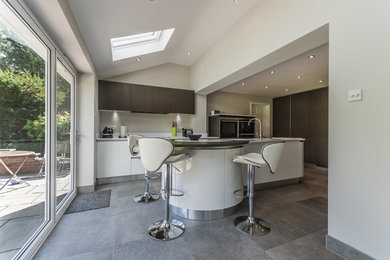 Photo of a large contemporary l-shaped open plan kitchen in Cheshire with a double-bowl sink, flat-panel cabinets, white cabinets, solid surface benchtops, white splashback, stainless steel appliances, porcelain floors and with island.